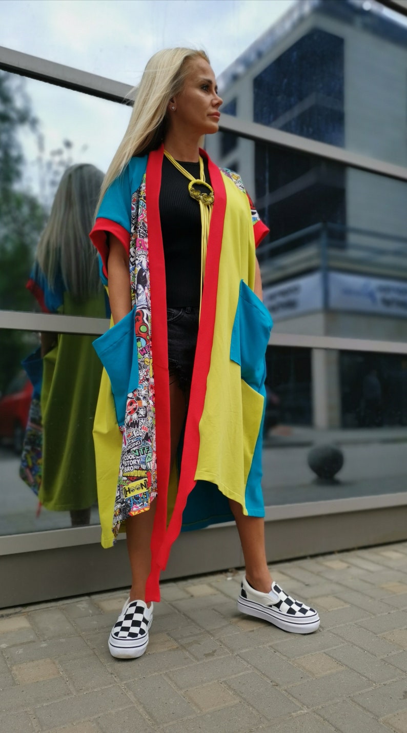 Może przedstawiać: Kobieta w kolorowej kurtce w stylu kimona w kolorze czerwonym, ż&oacute;łtym i niebieskim. Kurtka ma graficzny nadruk wewnątrz i długi, płynny kr&oacute;j. Ma na sobie czarne spodenki i czarno-białe szachownice.
