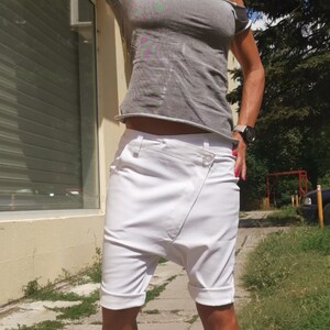 K&ouml;nnte beinhalten: Eine Frau tr&auml;gt ein graues, schulterfreies T-Shirt mit einer wei&szlig;en, kurzen, weiten Hose und wei&szlig;en Turnschuhen mit schwarzer "Chanel"-Beschriftung.