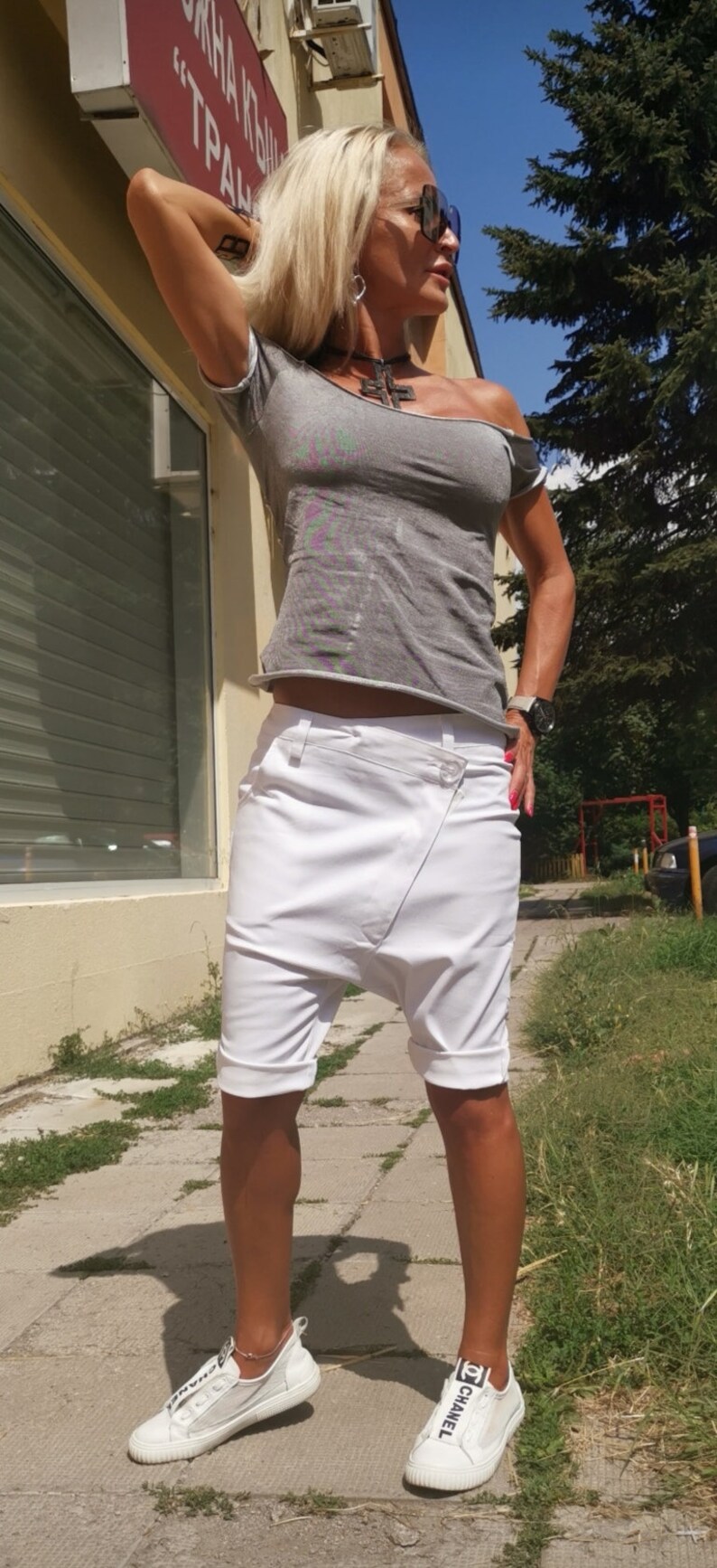 K&ouml;nnte beinhalten: Eine Frau tr&auml;gt ein graues, schulterfreies T-Shirt mit einer wei&szlig;en, kurzen, weiten Hose und wei&szlig;en Turnschuhen mit schwarzer "Chanel"-Beschriftung.