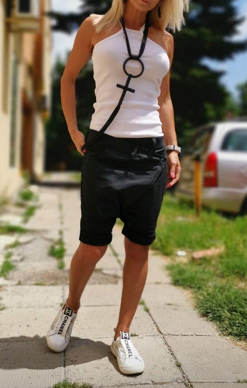 K&ouml;nnte beinhalten: Eine Frau tr&auml;gt ein wei&szlig;es Tanktop und schwarze Shorts mit einer schwarzen Kettenkette mit einem gro&szlig;en, runden Anh&auml;nger. Sie tr&auml;gt wei&szlig;e Turnschuhe mit schwarzer "CHANEL"-Beschriftung an den Seiten.