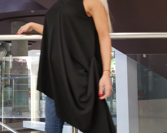 Puede incluir: Una mujer lleva una blusa negra asimétrica con un dobladillo largo y fluido. Lleva pantalones vaqueros azules y zapatillas negras y blancas con estampado gráfico. Las zapatillas tienen cordones blancos.