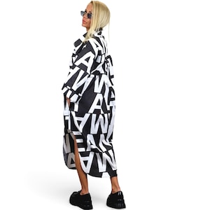 May include: A long-sleeved, calf-length shirt dress featuring a bold, all-over black and white graphic print consisting of large, repeating capital letters. The garment has a collared neckline, a button-down front, and a high-low hemline design.