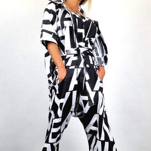 May include: A black and white patterned jumpsuit with a black belt and a black beret. The jumpsuit has a loose fit and wide legs. The person is wearing sunglasses.