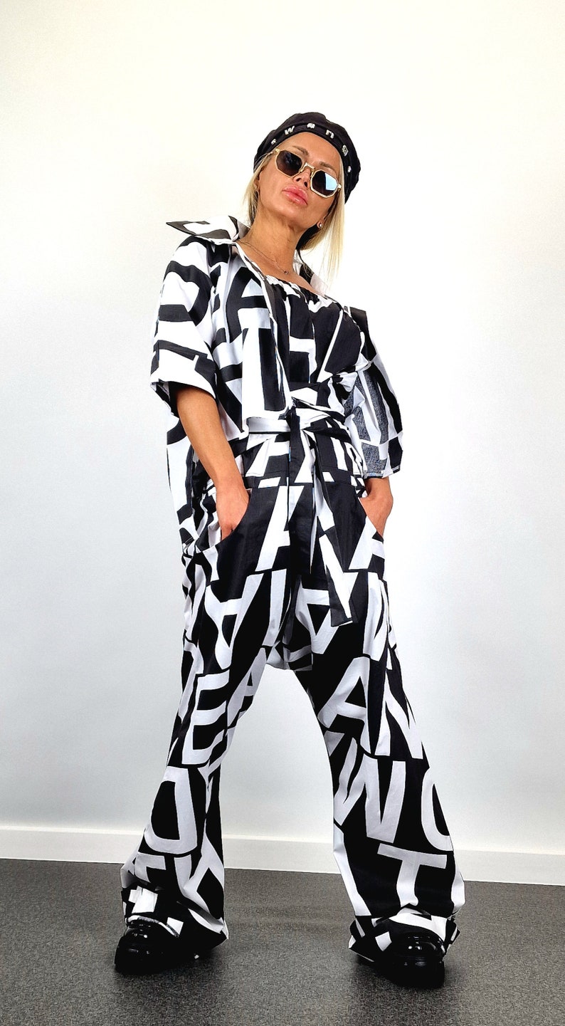 May include: A black and white patterned jumpsuit with a black belt and a black beret. The jumpsuit has a loose fit and wide legs. The person is wearing sunglasses.