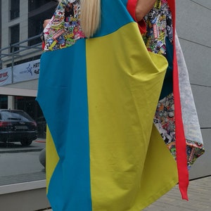 Może przedstawiać: Kobieta w długiej, kolorowej tunice w niebiesko-ż&oacute;łto-czerwonej kolorystyce. Tunika ma graficzny nadruk z naklejkami i logo. Ma na sobie czarno-białe sznurowane buty.