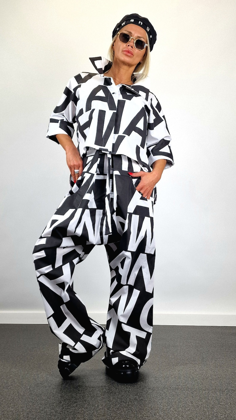 May include: A black and white patterned shirt and trousers set. The shirt has a button-up front and the trousers have a drawstring waist. The pattern is made up of large, bold letters.