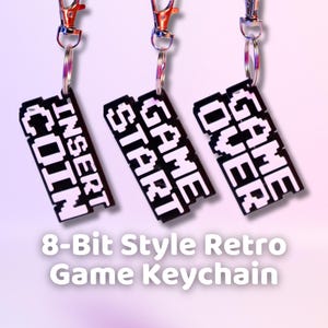 May include: Three black and white 8-bit style keychains with silver key rings. The keychains feature the text "GAME OVER", "GAME START", and "INSERT COIN".