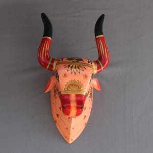 Pu&ograve; includere: Un decoro da parete in legno a forma di testa di toro dipinto a mano con corna nere, accenti rossi e arancioni e intricati motivi floreali.