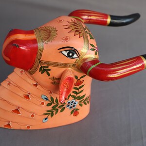 Pu&ograve; includere: Scultura di testa di toro in legno dipinta a mano con dettagli intricati. La testa del toro &egrave; dipinta in tonalit&agrave; di rosa, rosso e oro con motivi floreali. Le corna sono nere e rosse.
