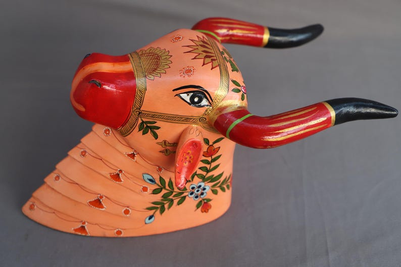 Pu&ograve; includere: Scultura di testa di toro in legno dipinta a mano con dettagli intricati. La testa del toro &egrave; dipinta in tonalit&agrave; di rosa, rosso e oro con motivi floreali. Le corna sono nere e rosse.