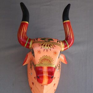 Pu&ograve; includere: Un decoro murale in legno a forma di testa di toro dipinto a mano con intricati motivi floreali in tonalit&agrave; arancio, rosso, giallo e verde. Le corna del toro sono nere con accenti rossi e dorati.