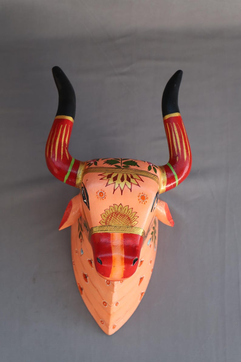 Pu&ograve; includere: Un decoro murale in legno a forma di testa di toro dipinto a mano con intricati motivi floreali in tonalit&agrave; arancio, rosso, giallo e verde. Le corna del toro sono nere con accenti rossi e dorati.