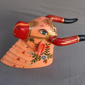 Pu&ograve; includere: Scultura di testa di toro in legno dipinta a mano con accenti rossi, neri e dorati. La testa del toro &egrave; decorata con motivi floreali e ha una base rosa.