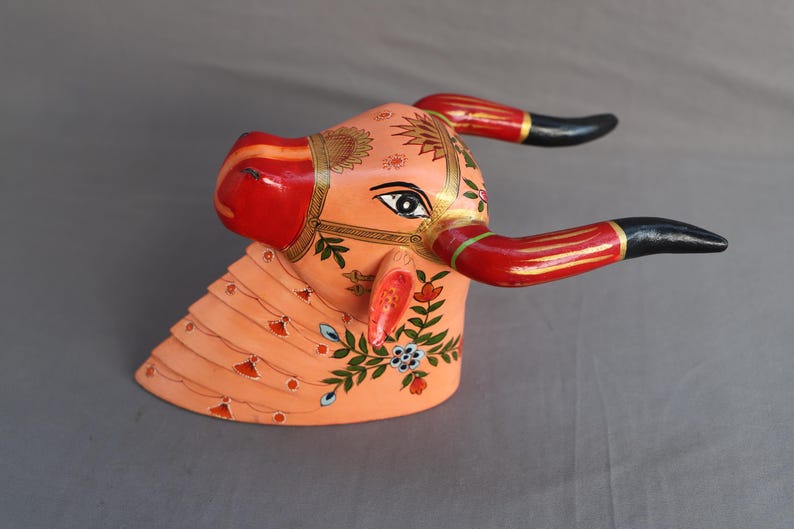 Pu&ograve; includere: Scultura di testa di toro in legno dipinta a mano con accenti rossi, neri e dorati. La testa del toro &egrave; decorata con motivi floreali e ha una base rosa.