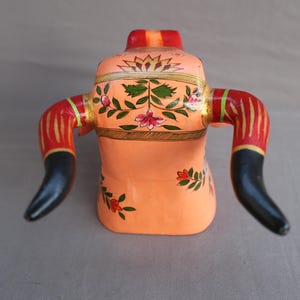 Pu&ograve; includere: Una statuetta di toro in legno dipinta a mano con corna nere, strisce rosse e dorate e motivi floreali in tonalit&agrave; rosa, verde e oro.