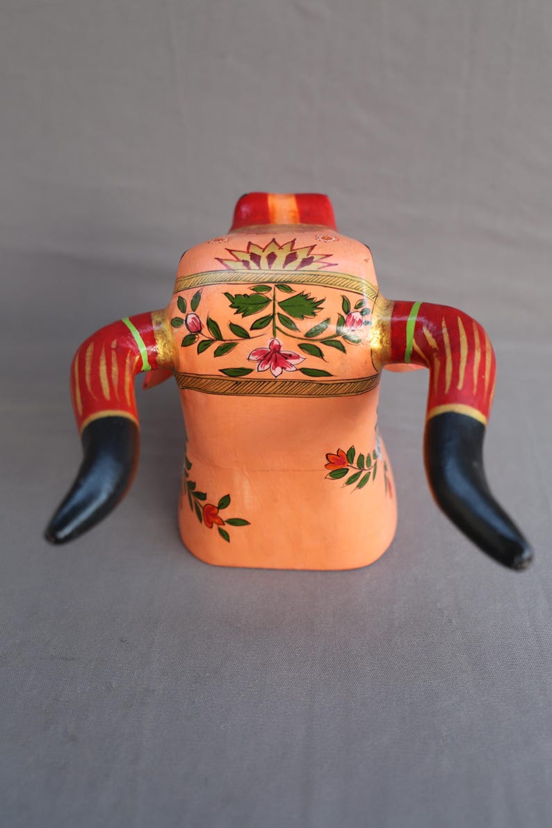 Pu&ograve; includere: Una statuetta di toro in legno dipinta a mano con corna nere, strisce rosse e dorate e motivi floreali in tonalit&agrave; rosa, verde e oro.