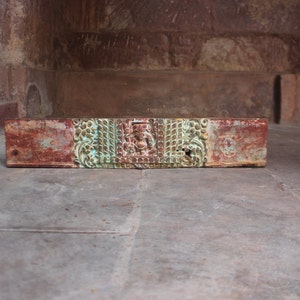 May include: A weathered wooden box with intricate carvings and a faded red, green, and gold paint finish. The box is sitting on a stone floor.