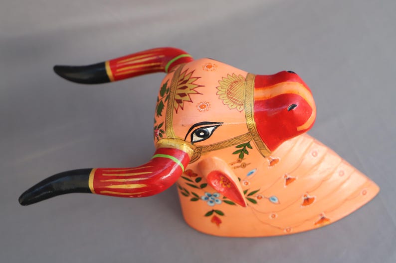 Pu&ograve; includere: Scultura di testa di toro in legno dipinta a mano con dettagli intricati. La testa del toro &egrave; dipinta in tonalit&agrave; di rosa, rosso e oro con motivi floreali. Le corna sono nere con strisce rosse e dorate.