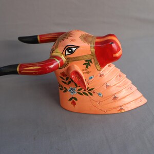 Pu&ograve; includere: Una scultura di testa di toro in legno dipinta a mano con corna nere, rosse e dorate. Il viso del toro &egrave; dipinto in tonalit&agrave; di rosa e arancio con motivi floreali e accenti blu.