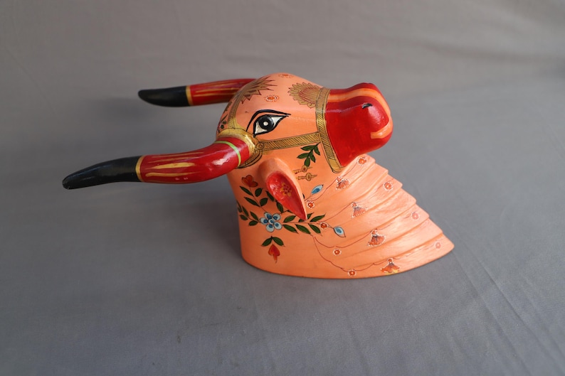 Pu&ograve; includere: Una scultura di testa di toro in legno dipinta a mano con corna nere, rosse e dorate. Il viso del toro &egrave; dipinto in tonalit&agrave; di rosa e arancio con motivi floreali e accenti blu.