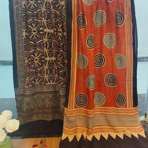 May include: Two cotton scarves with block printed designs. One scarf is black with a geometric pattern and the other is orange with a circle pattern.
