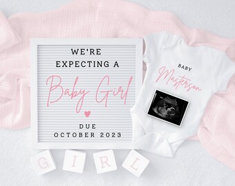 May include: A white letter board with the text "We're expecting a Baby Girl" in black lettering with a pink heart. The text "Due October 2023" is also in black lettering. A white onesie with the text "Baby Masterson" in pink lettering and a black and white ultrasound image is on top of a pink blanket. Four white blocks with the letters "GIRL" in pink lettering are in the bottom left corner of the image.
