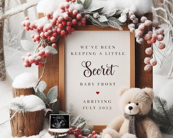 May include: A framed winter-themed pregnancy announcement with a teddy bear, a red heart, and the text "We've been keeping a little Secret Baby Frost Arriving July 2025".