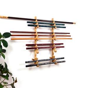 May include: A wooden chopstick holder with multiple pairs of chopsticks in various colors. The chopsticks are arranged horizontally on a light-colored wooden rack mounted on a white wall. The chopsticks are shades of brown, red, green, and black.