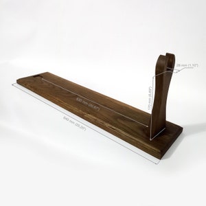 May include: A dark brown wooden display stand with a rectangular base and a curved support. The stand is 640 mm long, 530 mm wide, and 170 mm tall. The support is 28 mm thick.