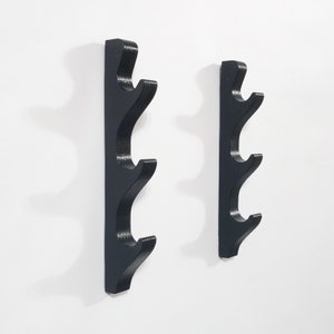 May include: Two black wall-mounted sword racks with four curved hooks each. The racks are made of wood and have a simple, modern design.