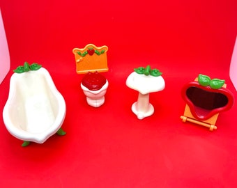 May include: A set of four miniature bathroom fixtures in a strawberry theme. The set includes a bathtub, toilet, sink, and mirror. The fixtures are made of plastic and are painted in white, red, and green.