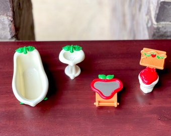 May include: A set of four miniature bathroom fixtures in white and green with a red and orange mirror. The set includes a bathtub, sink, toilet, and mirror.