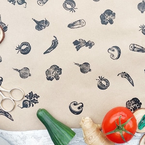 Puede incluir: Vista aérea de verduras frescas y sellos con ilustraciones de verduras sobre una superficie marrón. La imagen incluye cebollas rojas, tomates, un pepino, jengibre y sellos de madera con diseños de verduras.