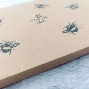 May include: A light brown box with a repeating pattern of black and yellow bumblebees. The text "Periwinkle Ink" is printed in black script. The box is angled, showing the top and side.