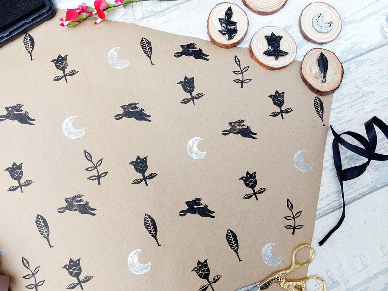 May include: Brown wrapping paper with a repeating pattern of black ink stamps. The stamps include a crescent moon, a leaf, a flower, and two rabbits running side by side.