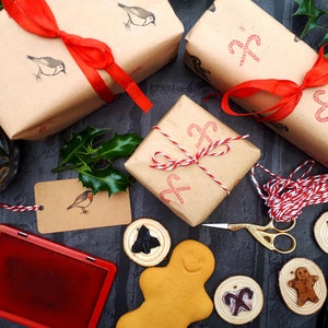 May include: Christmas-themed gift wrapping with brown paper, red ribbon, and stamps of birds and candy canes. Includes a red ink pad, gift tags, wooden ornaments, and a gingerbread man. Festive holiday decor.