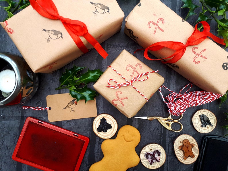 May include: Christmas-themed gift wrapping with brown paper, red ribbon, and stamps of birds and candy canes. Includes a red ink pad, gift tags, wooden ornaments, and a gingerbread man. Festive holiday decor.