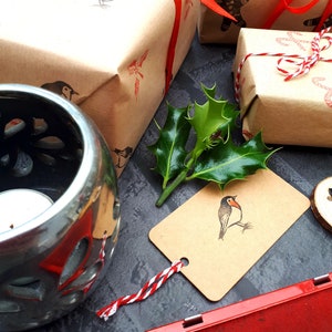 May include: Wrapped gifts with red ribbon and bird stamps. A silver candle holder, holly, and a red ink pad are also present. The gifts are wrapped in brown paper and tied with red ribbon.