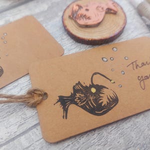 May include: A brown card with a black and white illustration of a anglerfish with a yellow lure. The card has the text "Thank you!" written on it.