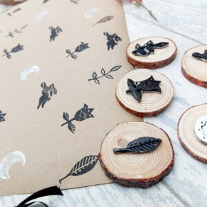 May include: A set of five wooden stamps with black and white designs. The designs include a crescent moon, a leaf, a flower, and two different rabbits. The stamps are on a brown paper background.