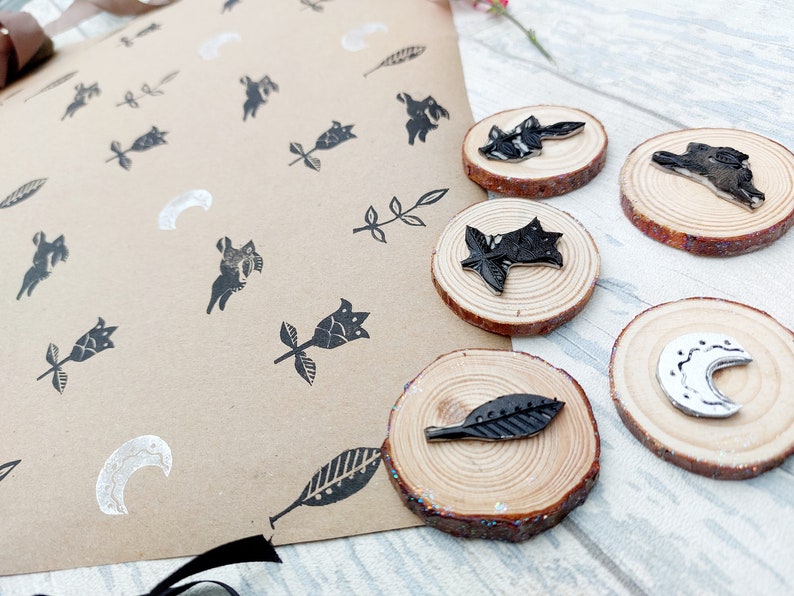 May include: A set of five wooden stamps with black and white designs. The designs include a crescent moon, a leaf, a flower, and two different rabbits. The stamps are on a brown paper background.