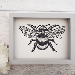 Puede incluir: Una l&aacute;mina art&iacute;stica enmarcada que presenta una ilustraci&oacute;n en tinta negra de un abejorro con patrones detallados en las alas sobre un fondo blanco. La obra est&aacute; contenida en un marco rectangular gris claro, sencillo y de perfil plano.