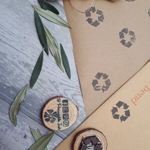 May include: Two wooden round slices with a brown background. One slice has a black and white recycle symbol and the other has a black and white swirl design. Both slices have a glittery blue finish. The background is brown paper with a recycle symbol printed on it.