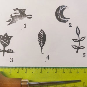 May include: Five different woodblock printing stamps, numbered 1 through 5. The stamps are on a white surface. The stamps depict a rabbit, a crescent moon, a flower, a leaf, and a branch with leaves.