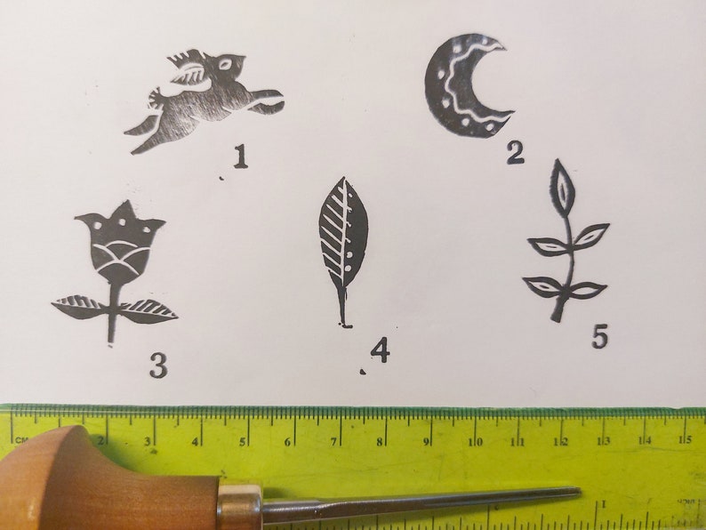 May include: Five different woodblock printing stamps, numbered 1 through 5. The stamps are on a white surface. The stamps depict a rabbit, a crescent moon, a flower, a leaf, and a branch with leaves.