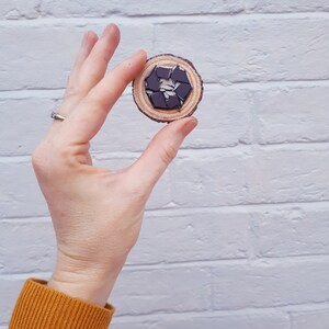May include: A wooden circle with a black and white recycle symbol in the center. The circle is being held by a hand against a white brick wall.