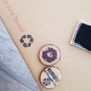 May include: Two wooden round stamps with a brown background. The first stamp has a black and white recycle symbol. The second stamp has a black and white logo with the text "AMPO" and "@Perishable Ink".