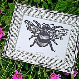 Puede incluir: Un grabado en lin&oacute;leo en blanco y negro de un abejorro dentro de un marco rectangular con un patr&oacute;n de rayas. La impresi&oacute;n presenta el texto escrito a mano "Bumble bee" en la parte inferior, junto al n&uacute;mero "1/50" y las iniciales "AF 2020".