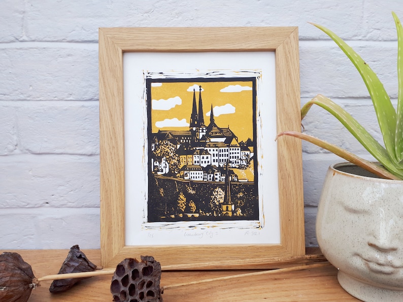 May include: A framed black and yellow linocut print of a cityscape with a church in the background. The print is titled "Linocut City" and dated "May 2021".