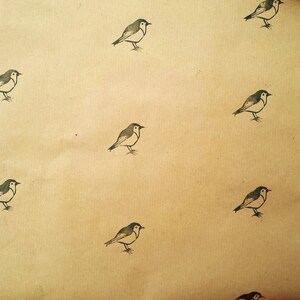 May include: Tan-colored paper with a repeating pattern of small, stylized birds. Each bird is depicted in black and white, with a simple, illustrative style. The birds are evenly spaced across the surface.